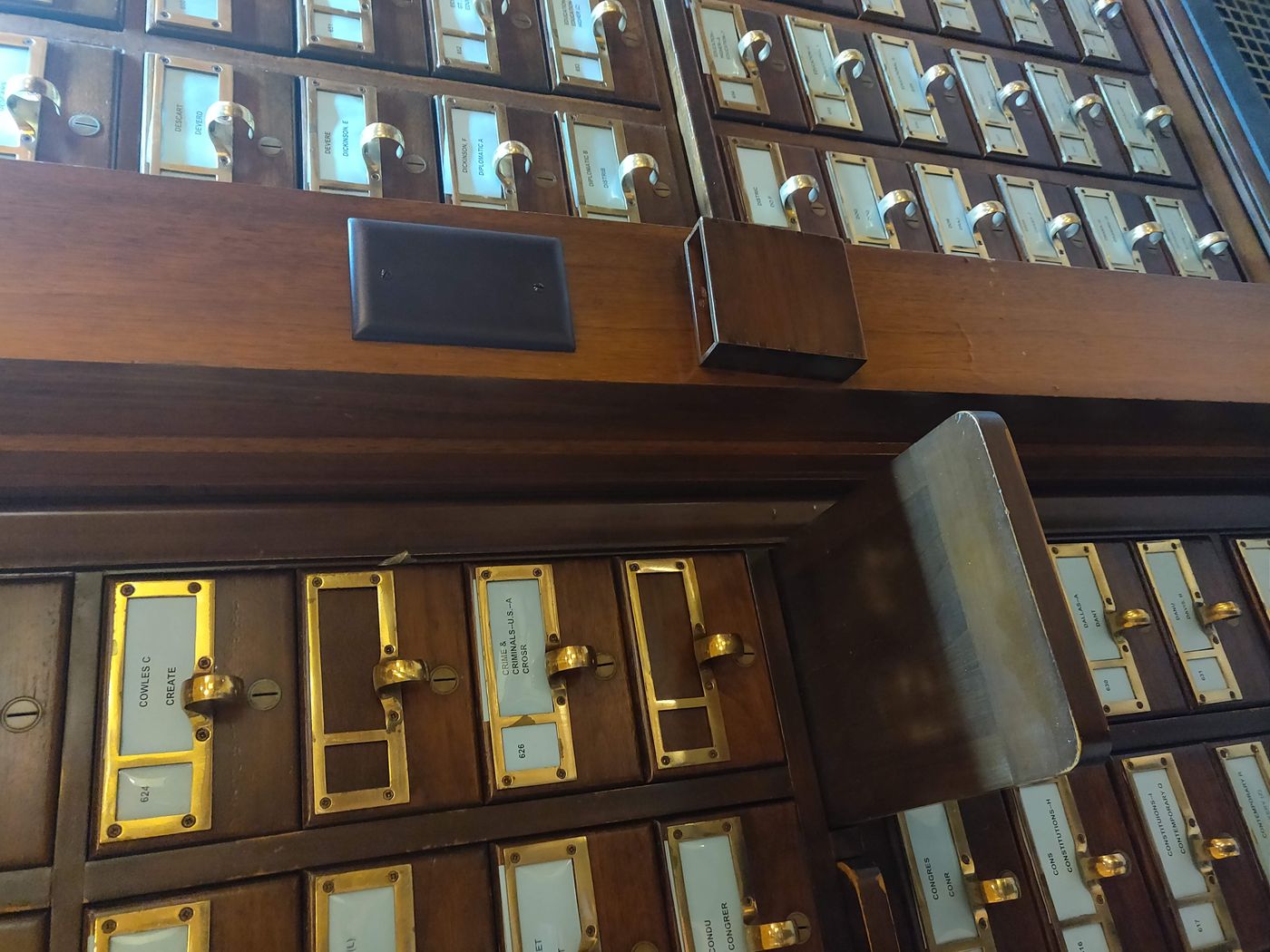Rows of wooden catalogue drawers in a library, each with a brass label holder and a round handle.