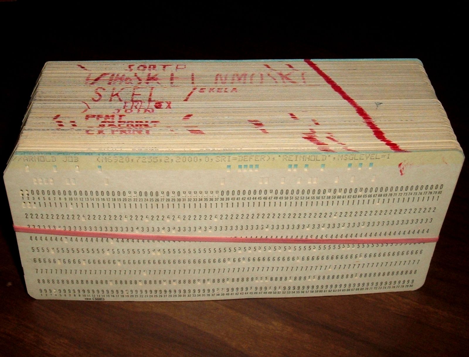 A stack of punched cards bound with a red elastic band, their printed numeric rows visible.